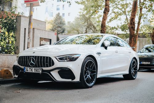 Free Sleek white luxury sedan parked on a tree-lined city street on a sunny day. Stock Photo