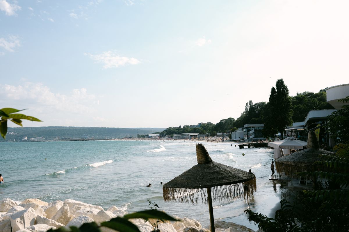 Plajă largă din Bulgaria cu umbrele de paie aliniate și un golf deschis în fundal