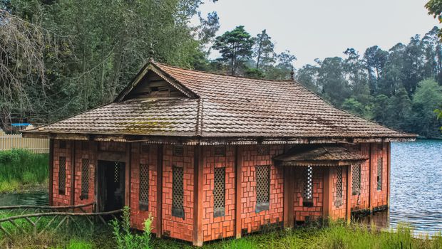 Traditional brick house beside serene lake in lush Kodaikanal landscape.
