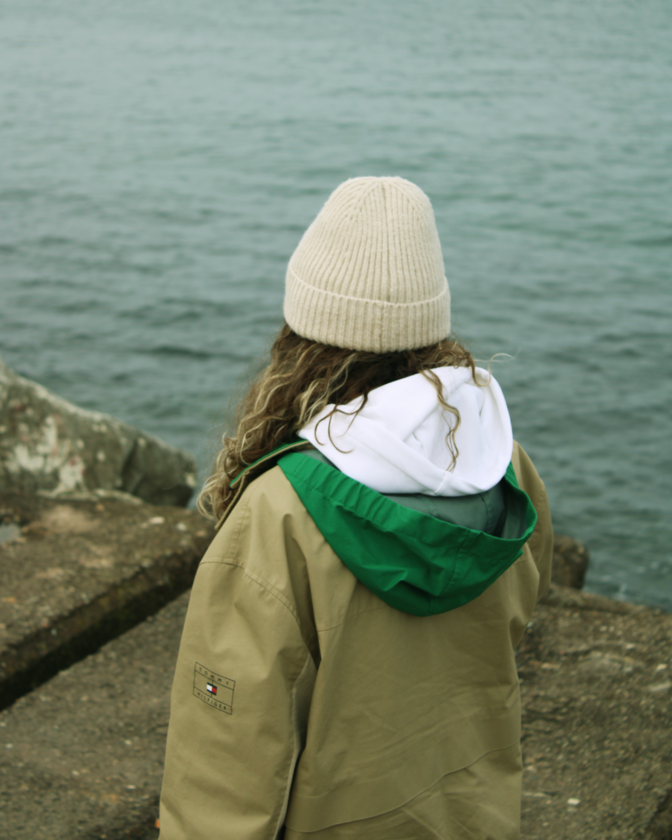 A woman in a beanie and winter coat gazes out at the ocean, capturing a serene moment.