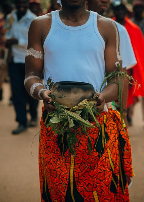 Free Man in vibrant attire holds pot with leaves at cultural festival. Stock Photo