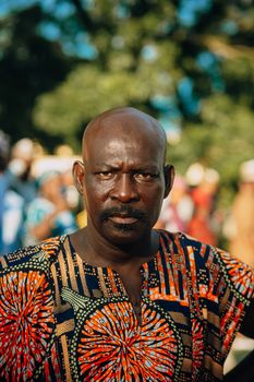 A serious adult man wearing colorful African print clothing outdoors.