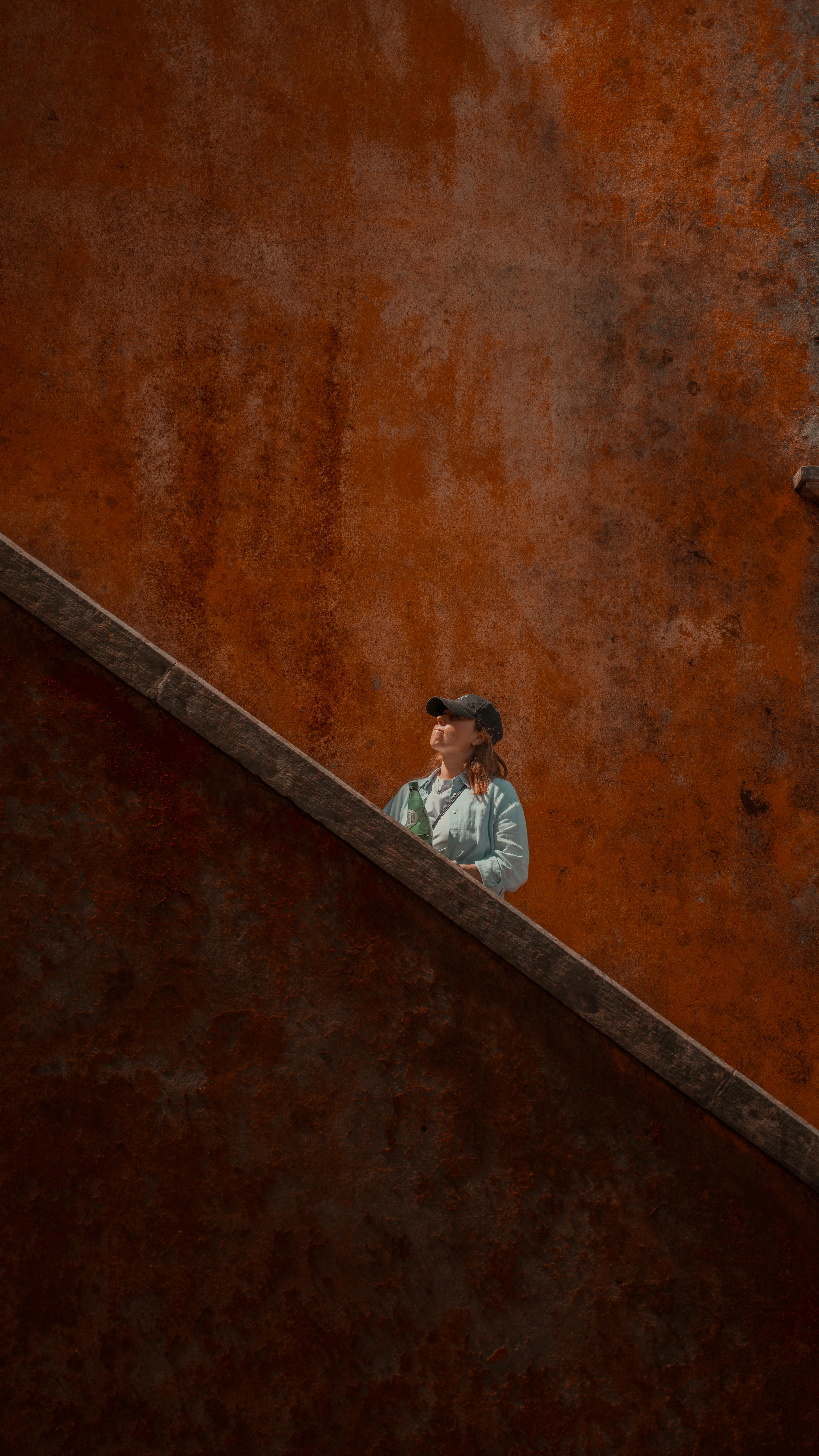 De franc Una persona amb gorra es troba en una escala rovellada a Lisboa, Portugal, amb un fons de textura taronja cridaner. Foto d'estoc