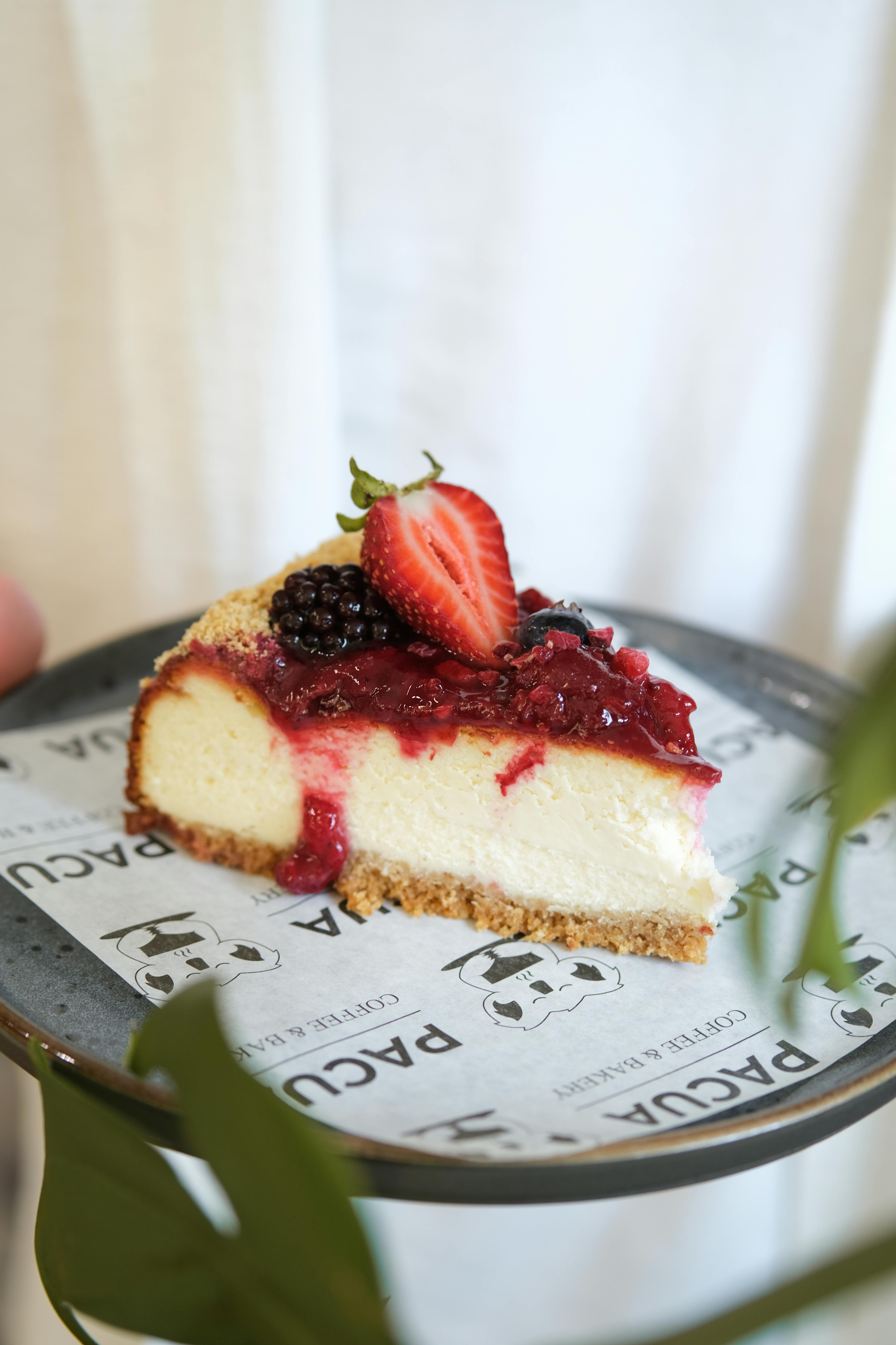 Slice of cheesecake topped with fresh strawberries, blackberries, and berry sauce on a decorative plate.