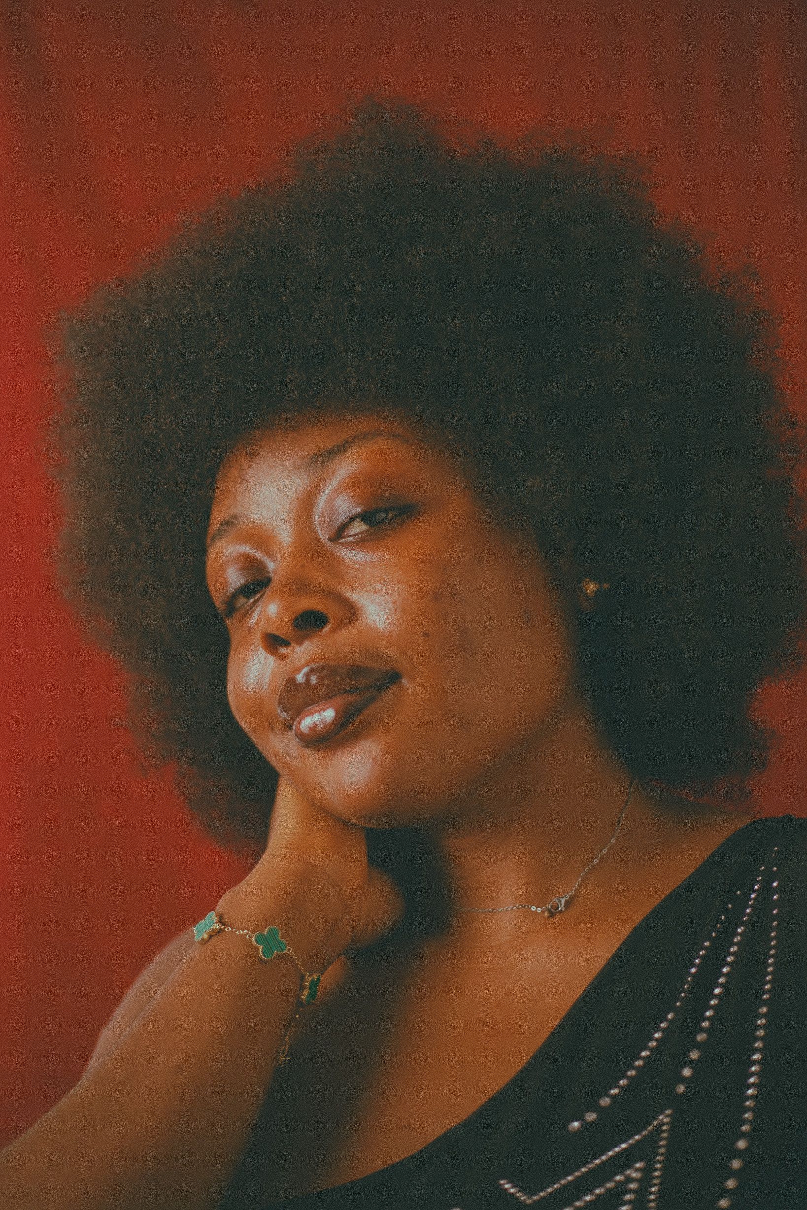 Stylish portrait of a woman with Afro hairstyle against a red backdrop, exuding confidence.