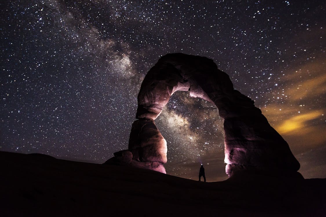 Free Person Standing Under A Rock Formation On A Starry Night Stock Photo