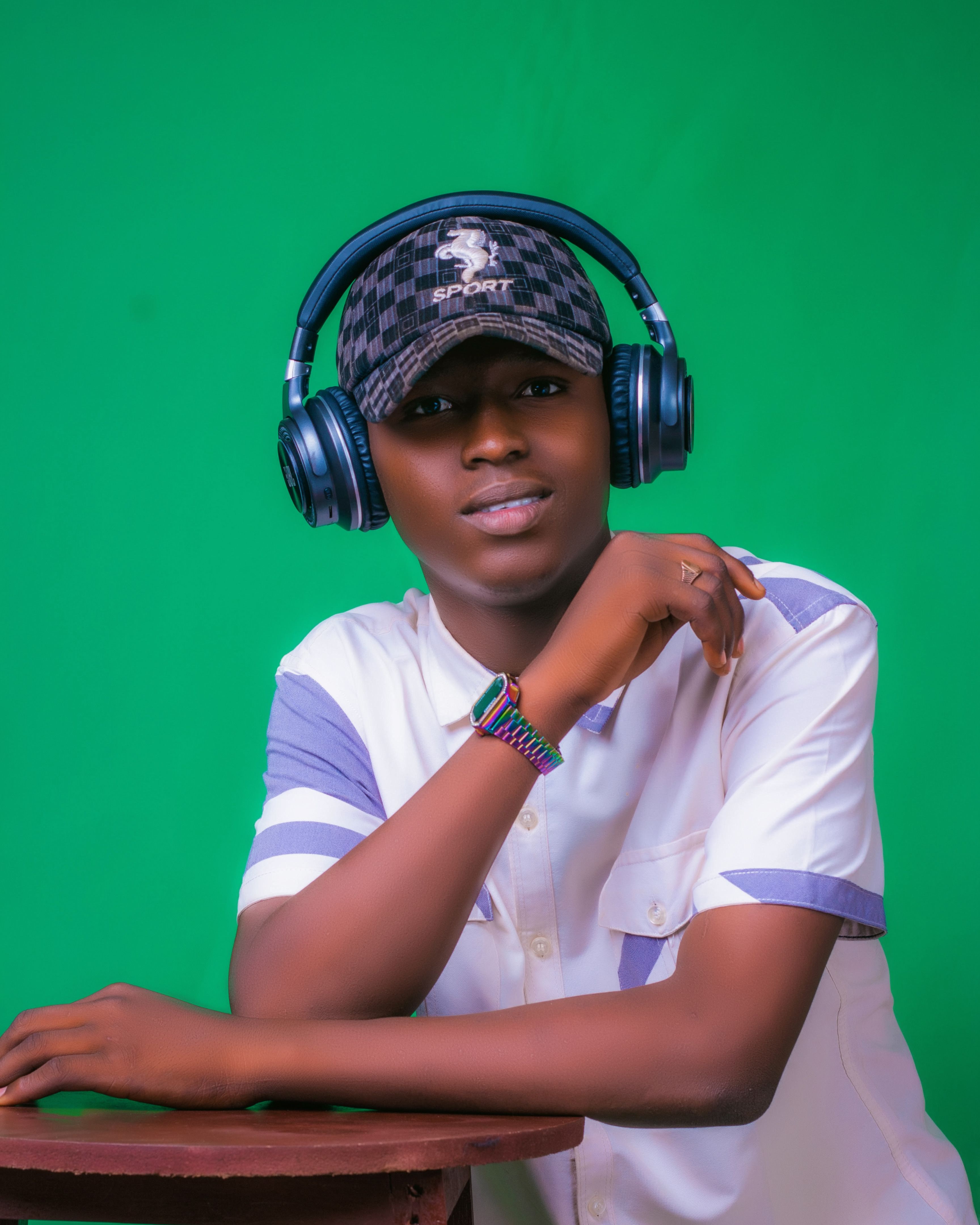 Confident young man wearing headphones and cap against green backdrop.