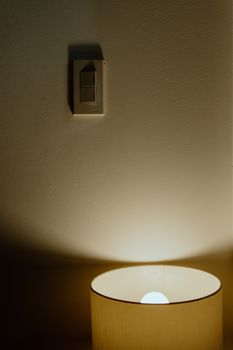 Warmly lit lamp illuminating a wall with a light switch, creating a serene ambiance.