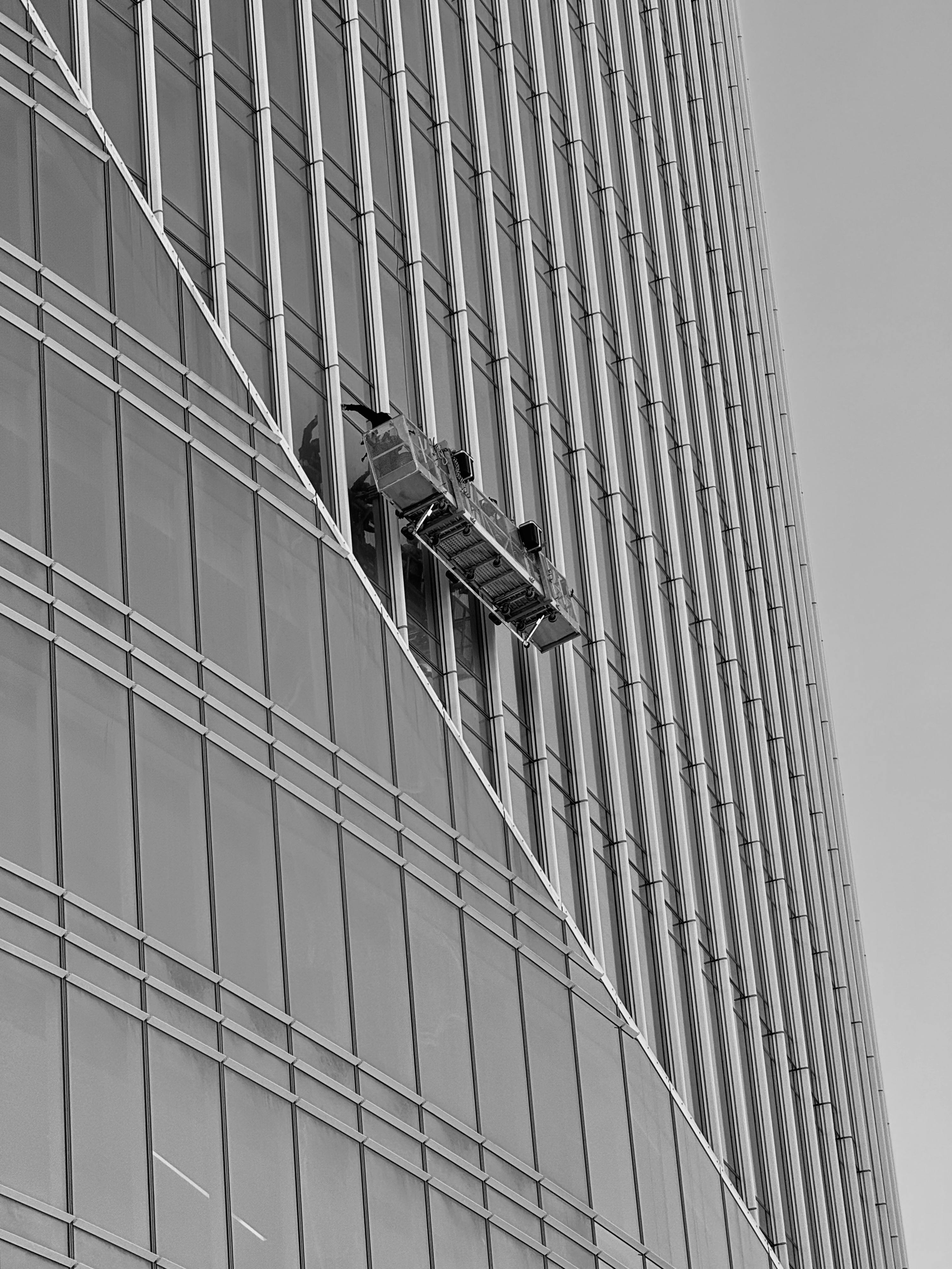 Kostenlos Fensterputzer auf einer Hängeplattform vor einem modernen Glaswolkenkratzer. Stock-Foto