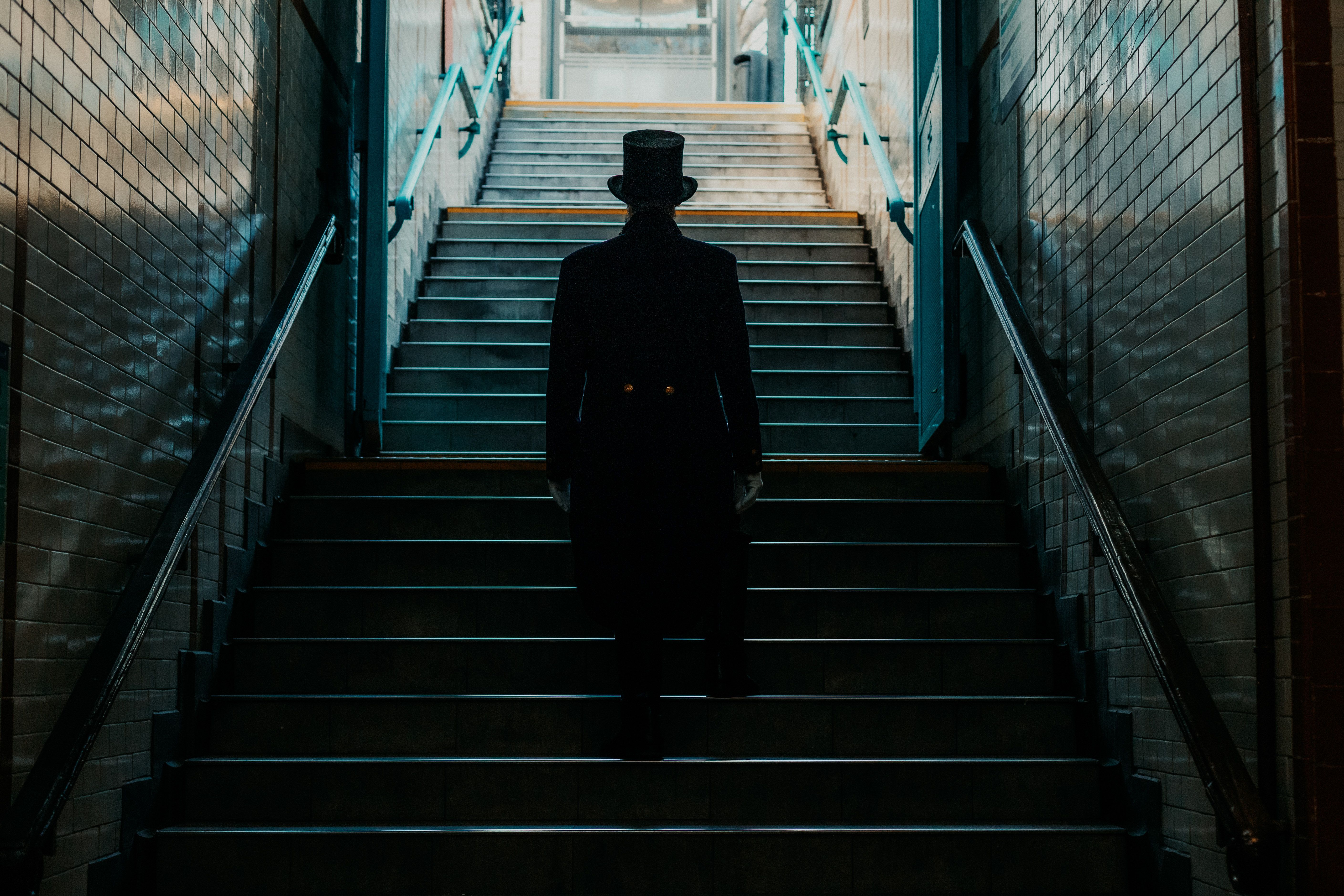 A shadowy figure in vintage attire ascends a dimly lit staircase in Buenos Aires.