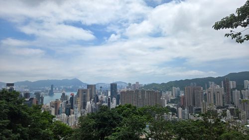 Free Stunning panoramic view of Hong Kong's skyline with distinctive skyscrapers and lush greenery under a cloudy sky. Stock Photo