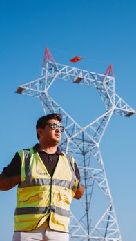 Engineer wearing safety vest inspects towering power lines on a sunny day.