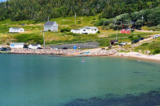 A picturesque Nova Scotia coastal village with beachgoers enjoying a sunny day by the sea.