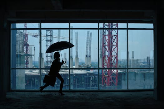 Silhouette of person with umbrella and briefcase running inside a building, overlooking construction site through large windows.