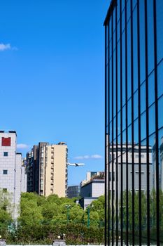 An airplane flies over a cityscape with modern glass buildings and clear blue sky.