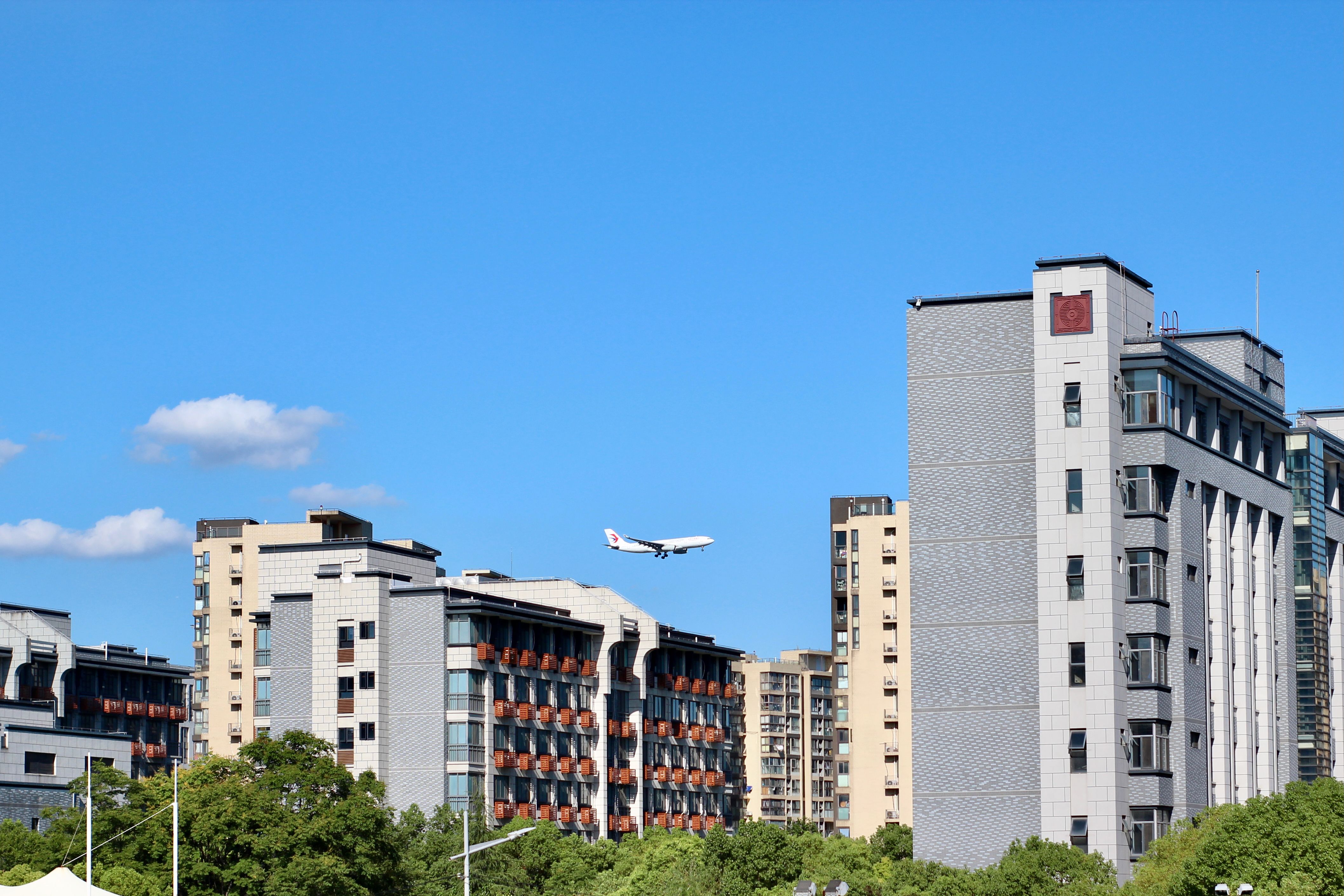 Airplane flying above urban buildings under a bright blue sky, symbolizing travel and urban life.