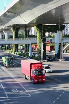 Red truck on a busy urban highway under a modern overpass with greenery.
