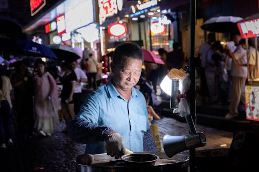 Street vendor in blue shirt cooks food at night in a bustling market.