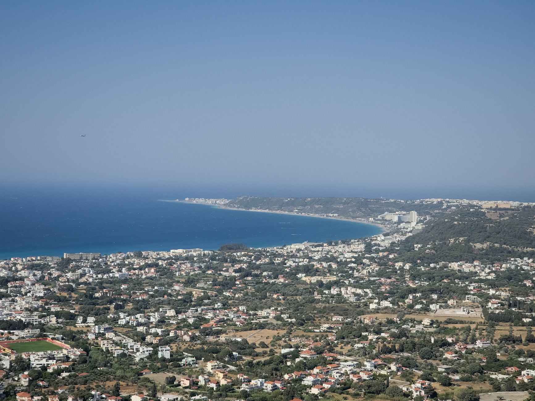 Stunning aerial view of a coastal cityscape and azure sea in Greece on a sunny day.
