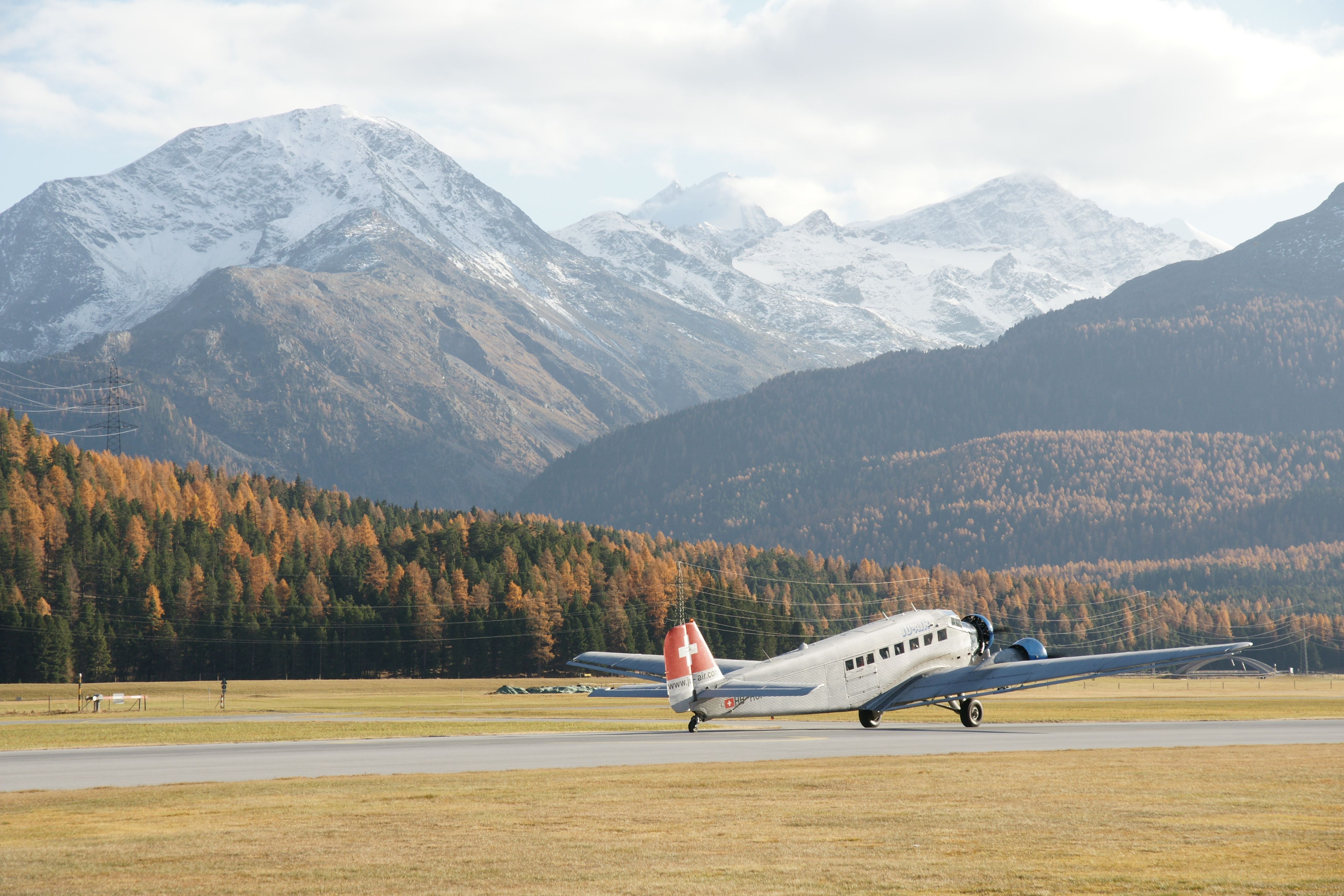 A vintage airplane takes off against the majestic backdrop of snowy alpine peaks.