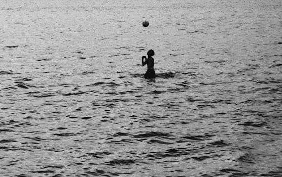 A child plays with a ball in the water, silhouetted against the serene backdrop of Hanoi, Vietnam.
