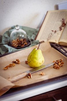 A pear and walnuts on a baking tray, styled with an open book.