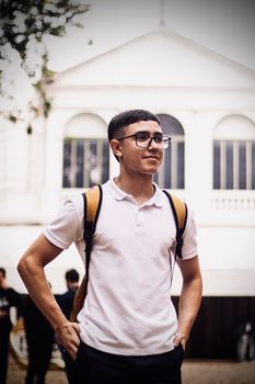 Confident young man with backpack outdoors in front of white building, urban lifestyle.