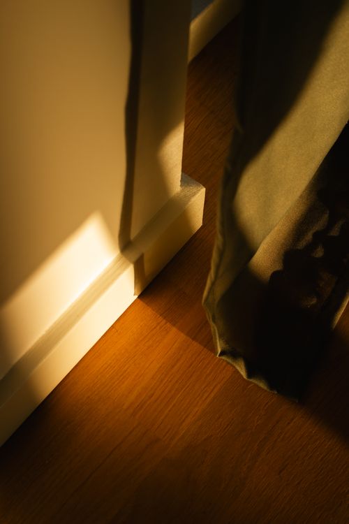 Free Warm sunlight casting shadows through a curtain onto a wooden floor. Stock Photo