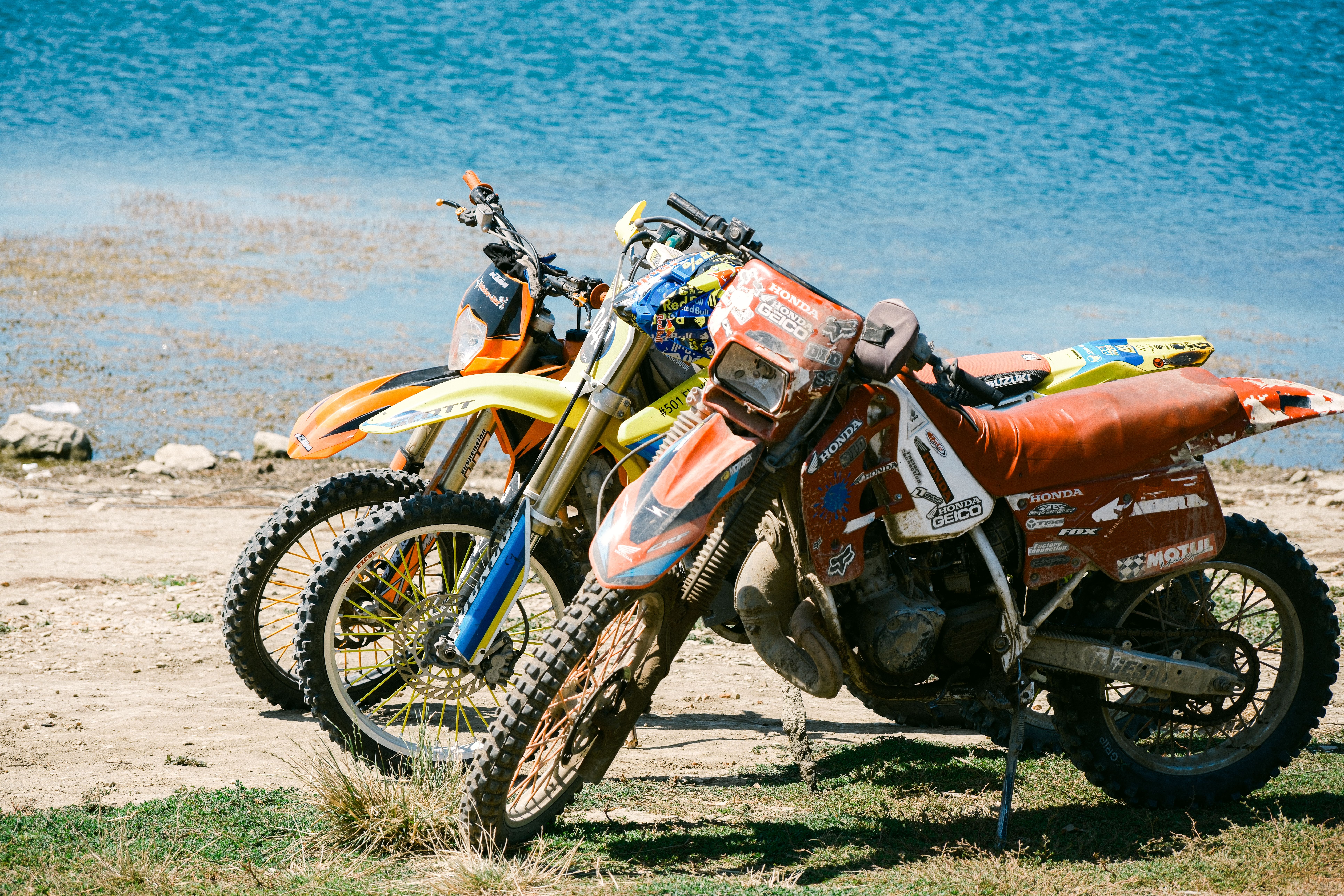 Two dirt bikes parked by the serene shoreline of Varna, Bulgaria, under a bright day.