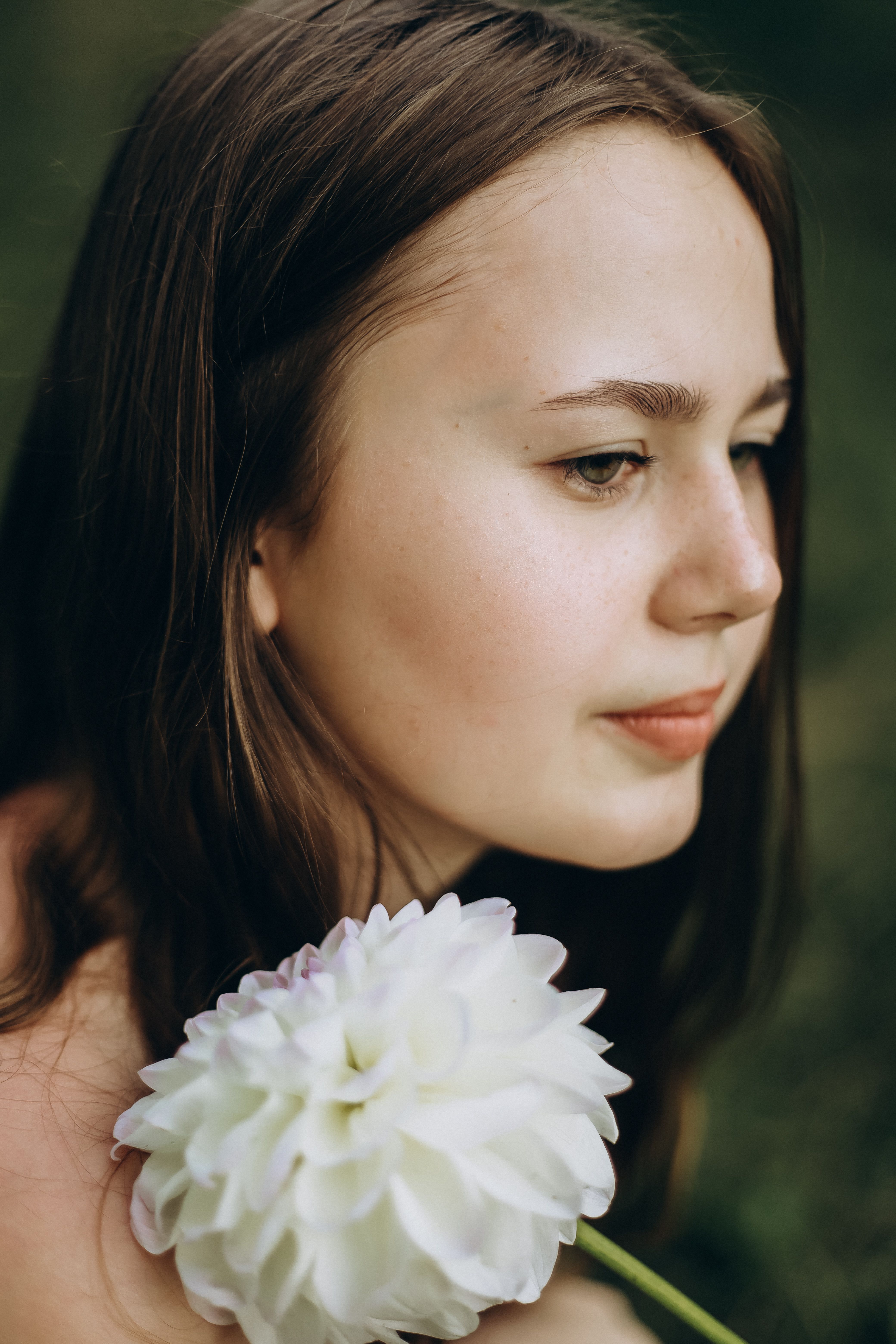 Young woman holding a white flower, serene naive expression, soft natural light