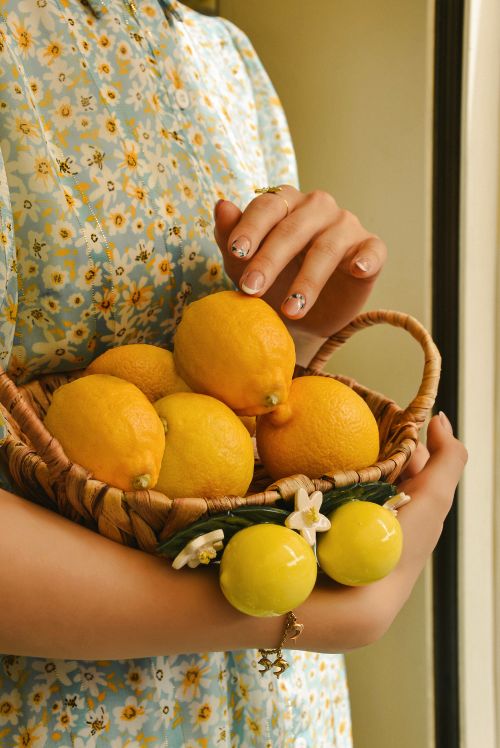 Free A woman in a floral dress holding a basket full of fresh lemons. Perfect for healthy lifestyle themes. Stock Photo