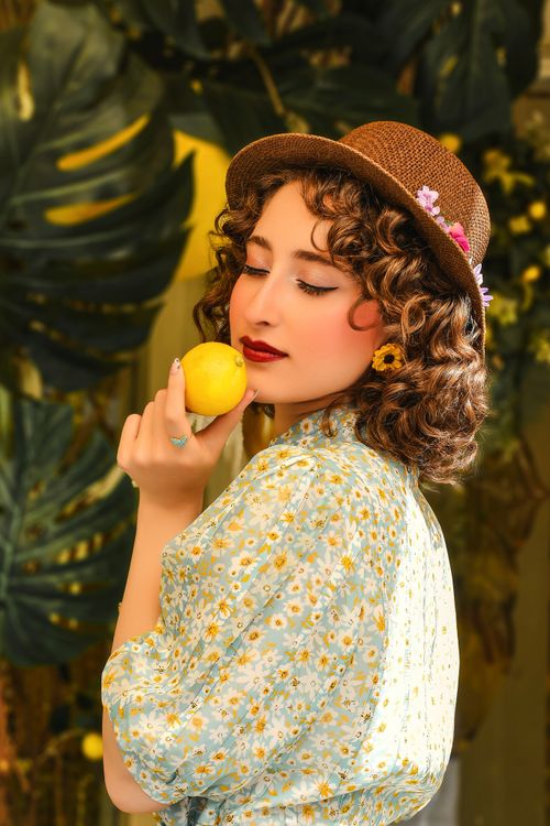 Free A woman in a stylish hat holds a lemon against a vibrant floral background. Stock Photo