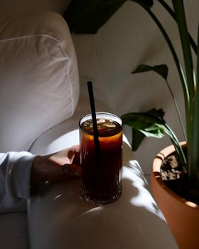 Relaxing indoors with a refreshing iced coffee beside lush greenery.