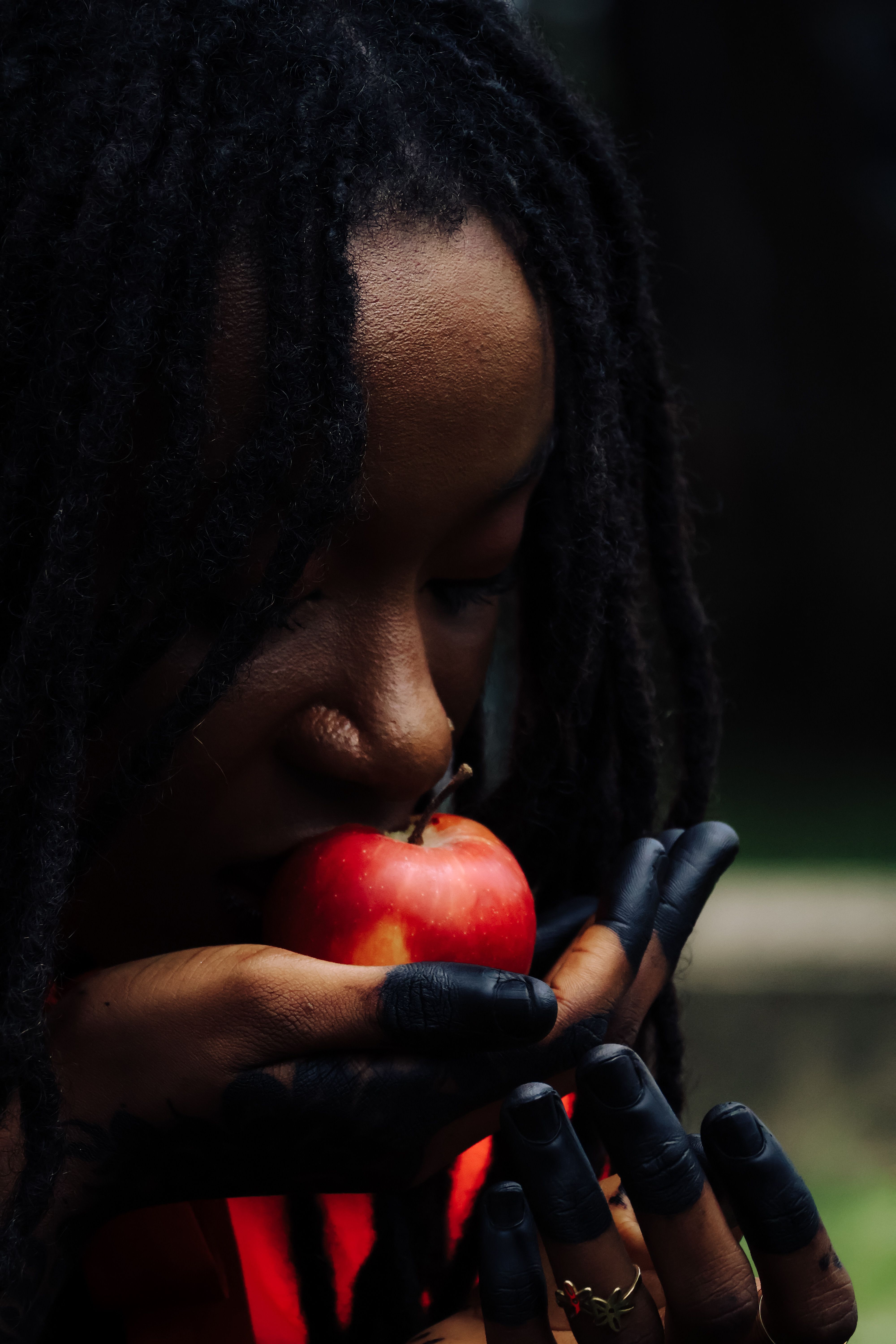 A contemplative woman holds a red apple in a lush outdoor setting.