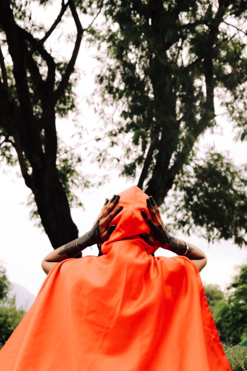 Free A person in a flowing red cloak stands with hands raised against a forest backdrop. Stock Photo