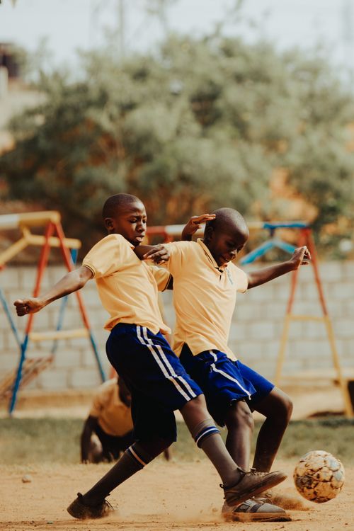 Free Two children energetically playing soccer in a Kampala schoolyard, capturing the joy and dynamism of youth sports. Stock Photo