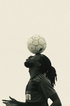 A skillful athlete balances a soccer ball in this artistic, high-contrast image.