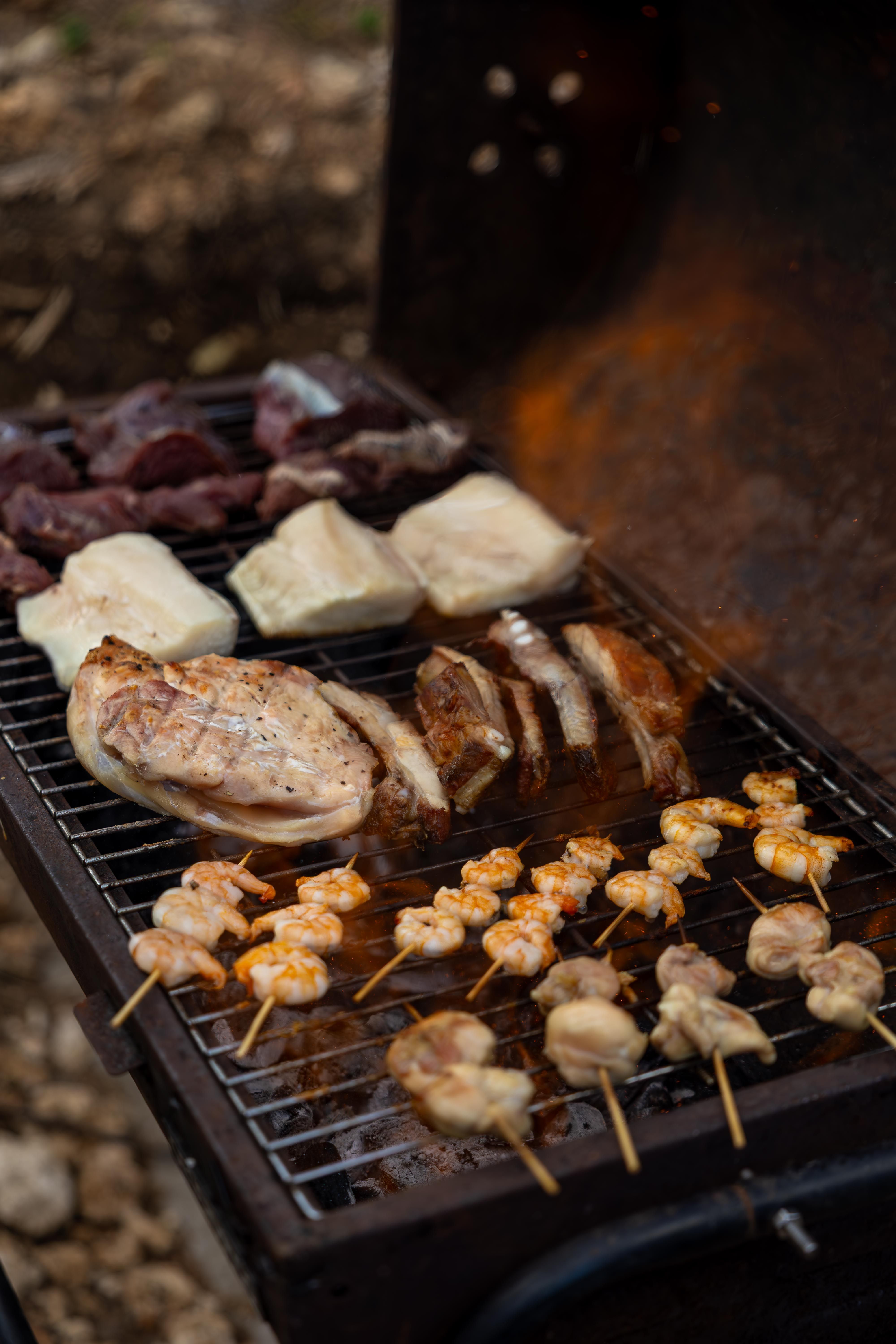 Tantalizing barbecue with various meats and shrimp skewers on the grill outdoors.