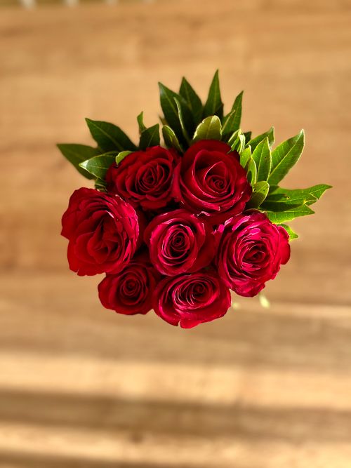 Free A vibrant bouquet of red roses with lush green leaves on a wooden background. Stock Photo