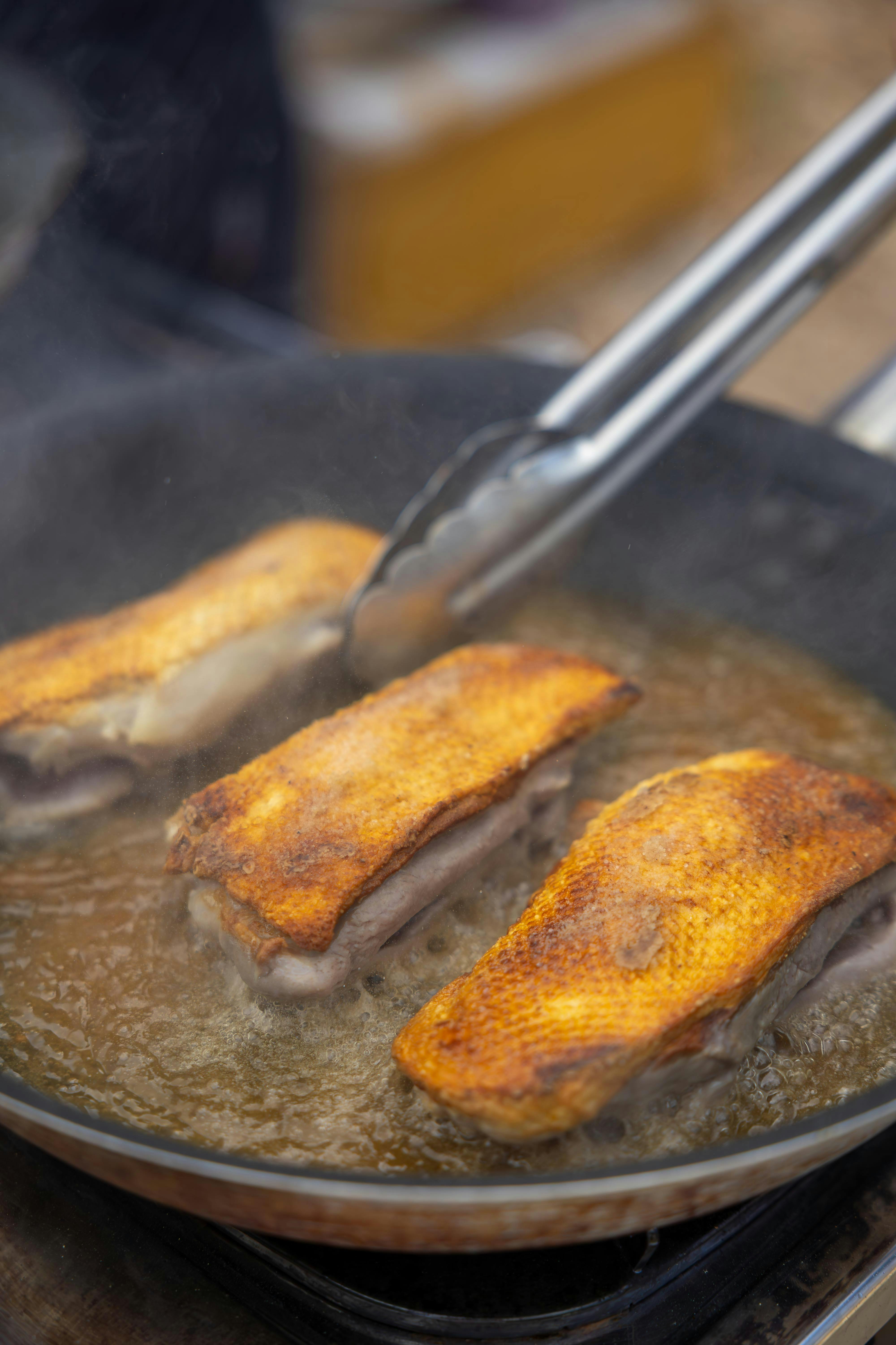 Sizzling duck breasts being cooked to perfection in a frying pan with tongs.