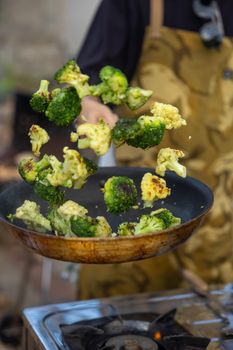 Fresh broccoli florets being tossed in a frying pan by a chef. Perfect for cooking and health themes.