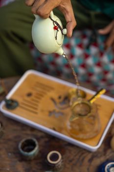 Close-up of a traditional tea pouring ceremony with an elegant teapot and bamboo tray.