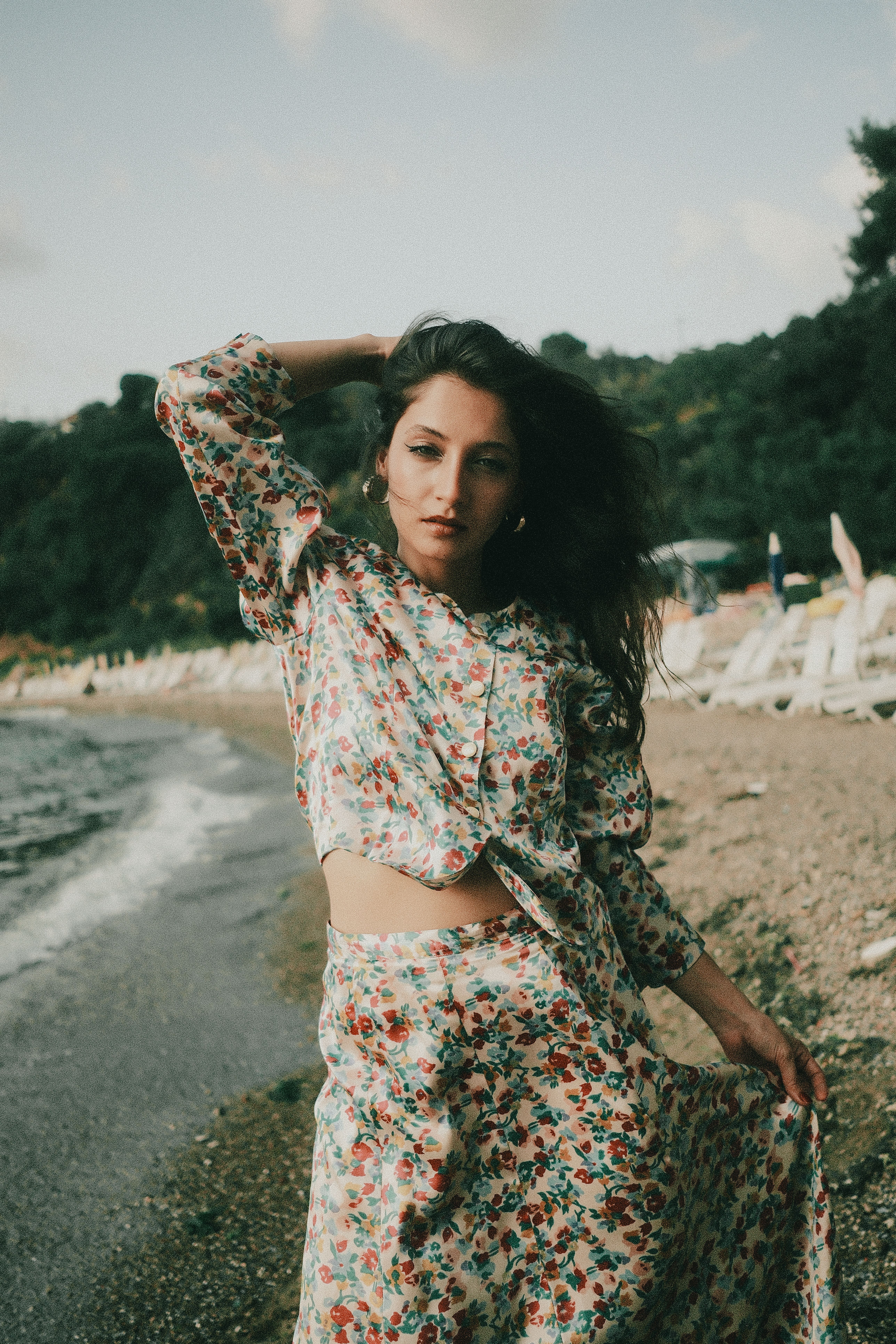 Woman in floral dress poses gracefully by the beach shore.
