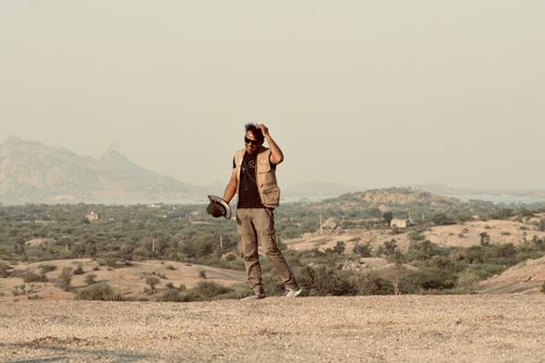 Free A man in adventure attire stands in a desert with a mountainous background. Stock Photo