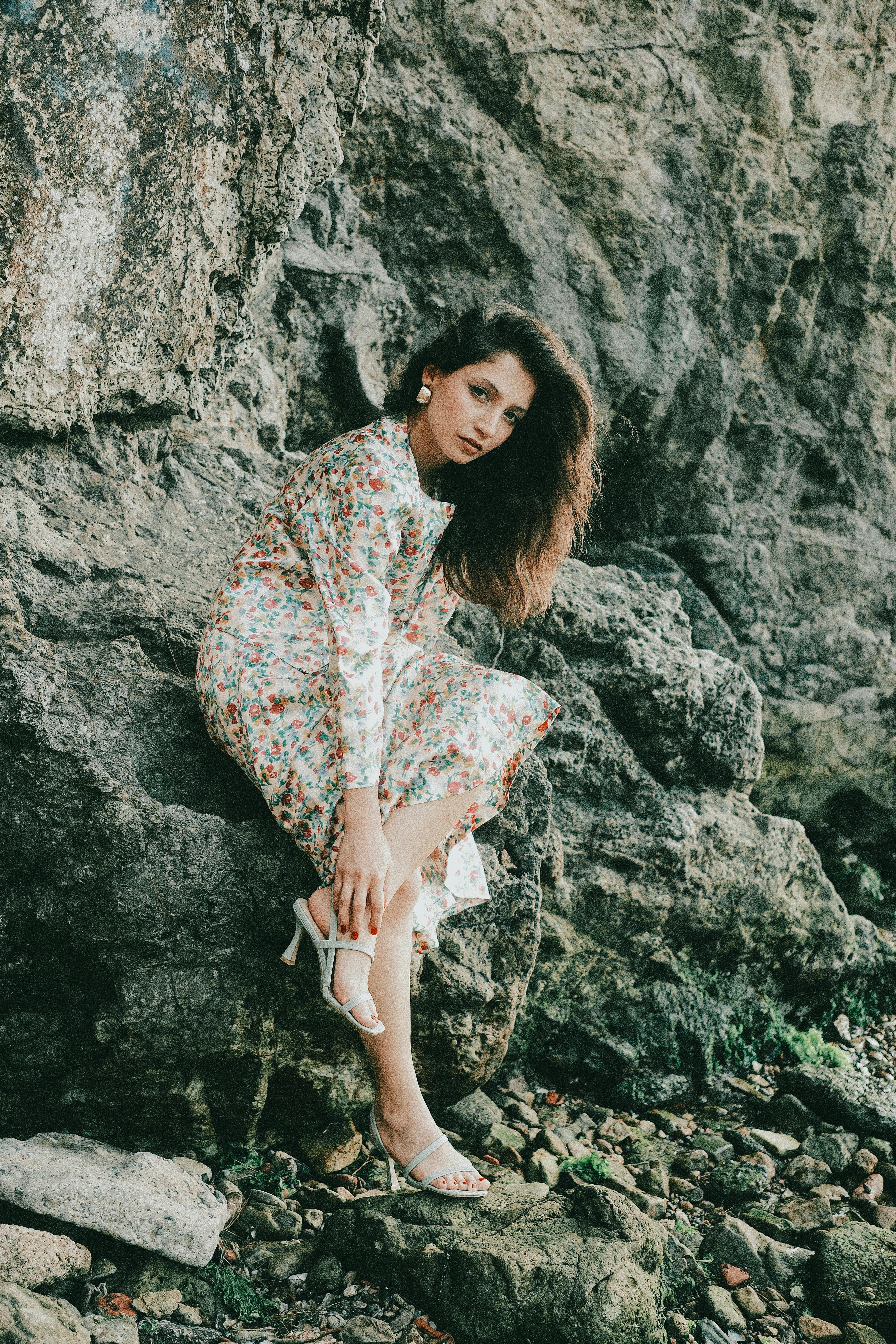 身穿花卉连衣裙的女子，坐在海边的岩石悬崖上，散发出宁静与自然之美