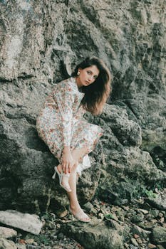 身穿花卉连衣裙的女子，坐在海边的岩石悬崖上，散发出宁静与自然之美