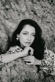 A thoughtful woman poses against a rock in a classic black and white portrait.