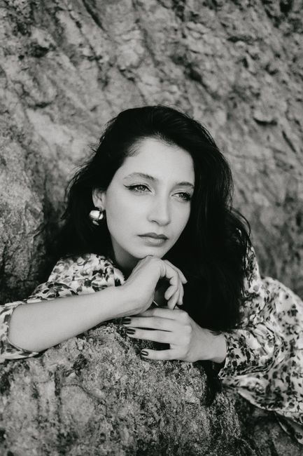 A thoughtful woman poses against a rock in a classic black and white portrait.