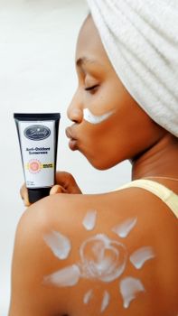 Woman with towel on head applying sunscreen on shoulder, holding tube.
