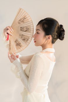 Portrait of an elegant woman holding a traditional Asian fan, showcasing delicate style and grace.